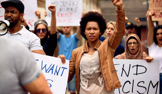 Protest image with young black woman in a canvas jacket raising her fist to the air in the black power sign along with other protesters. https://naacp.org/articles/fbi-annual-hate-crimes-report-incomplete